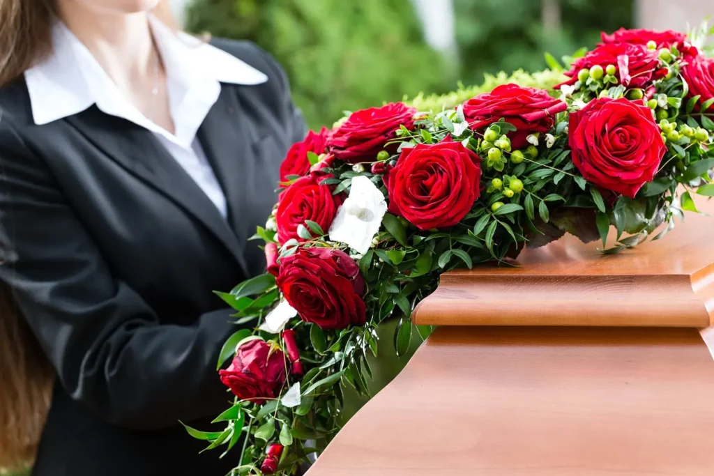 Détail de roses rouges ornant un cercueil en bois lors d'obsèques.