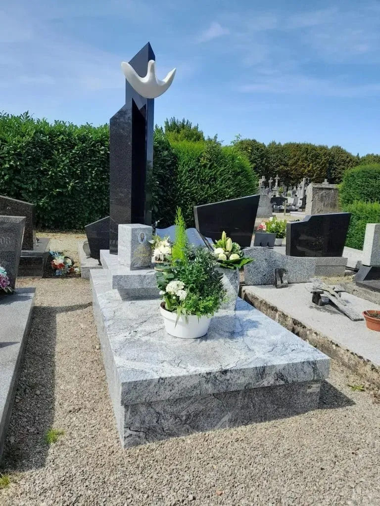 Tombe moderne en granit gris avec sculpture de colombe dans un cimetière.